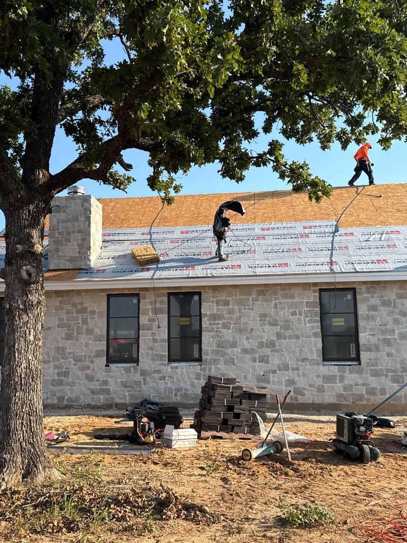 Roofer installing composite shake on a stone ranch home under a live oak