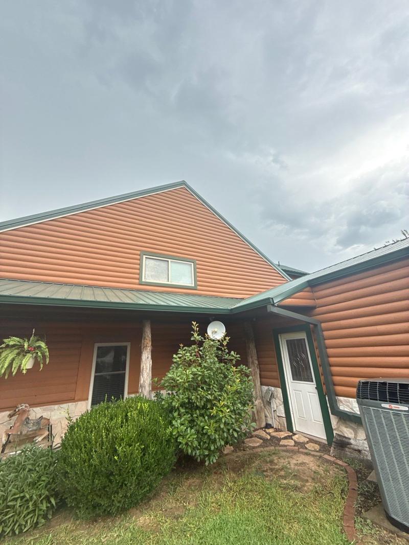 Green standing seam metal roof and trim over the porch of a log-look siding home