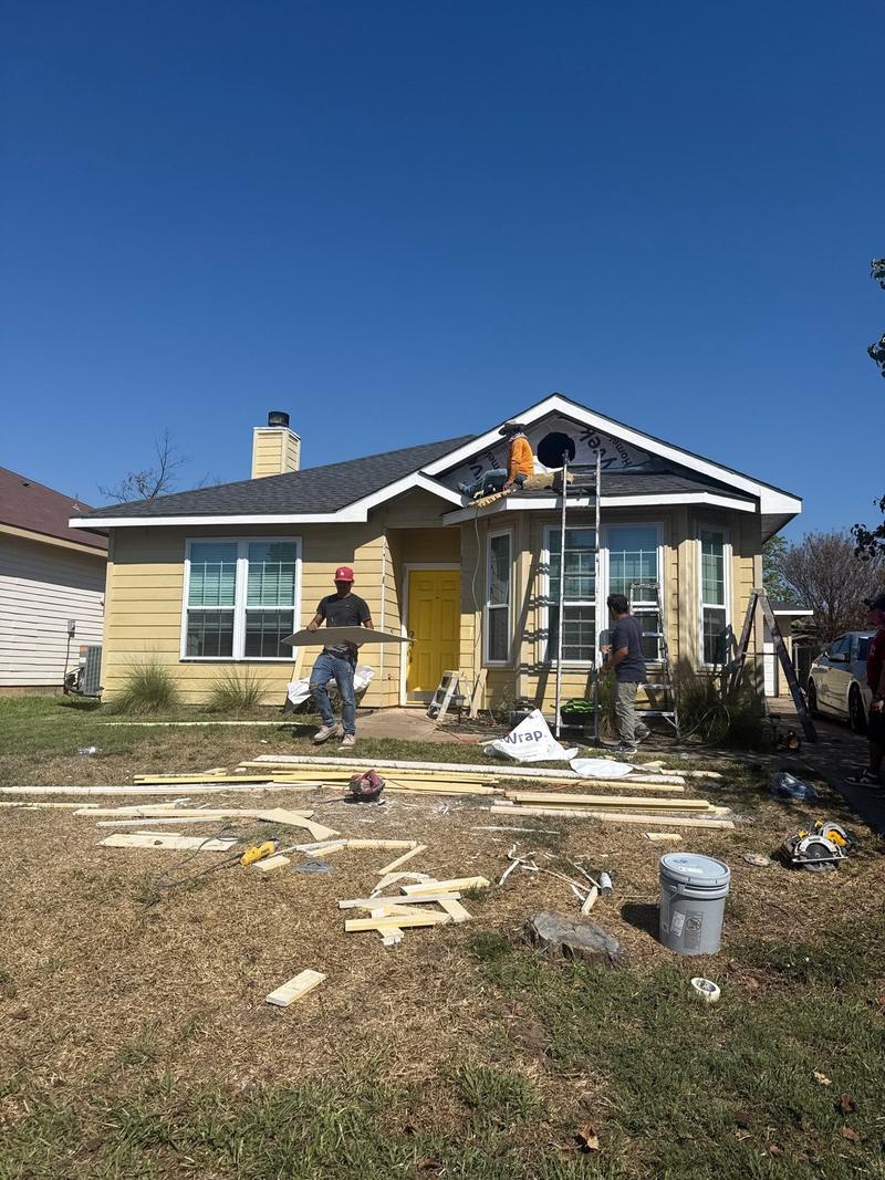 Snow Roofing & Exteriors crew replacing yellow lap siding on a one-story home, with house wrap exposed at the front gable