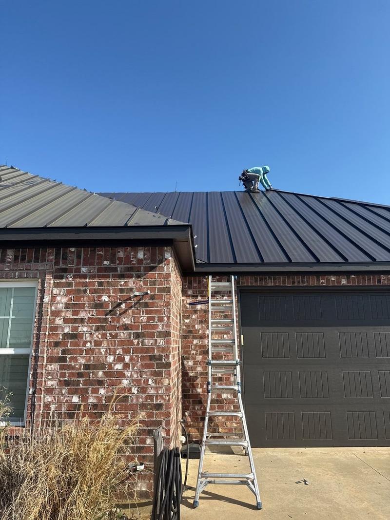 Roofer finishing standing seam panels at a hip on a brick garage